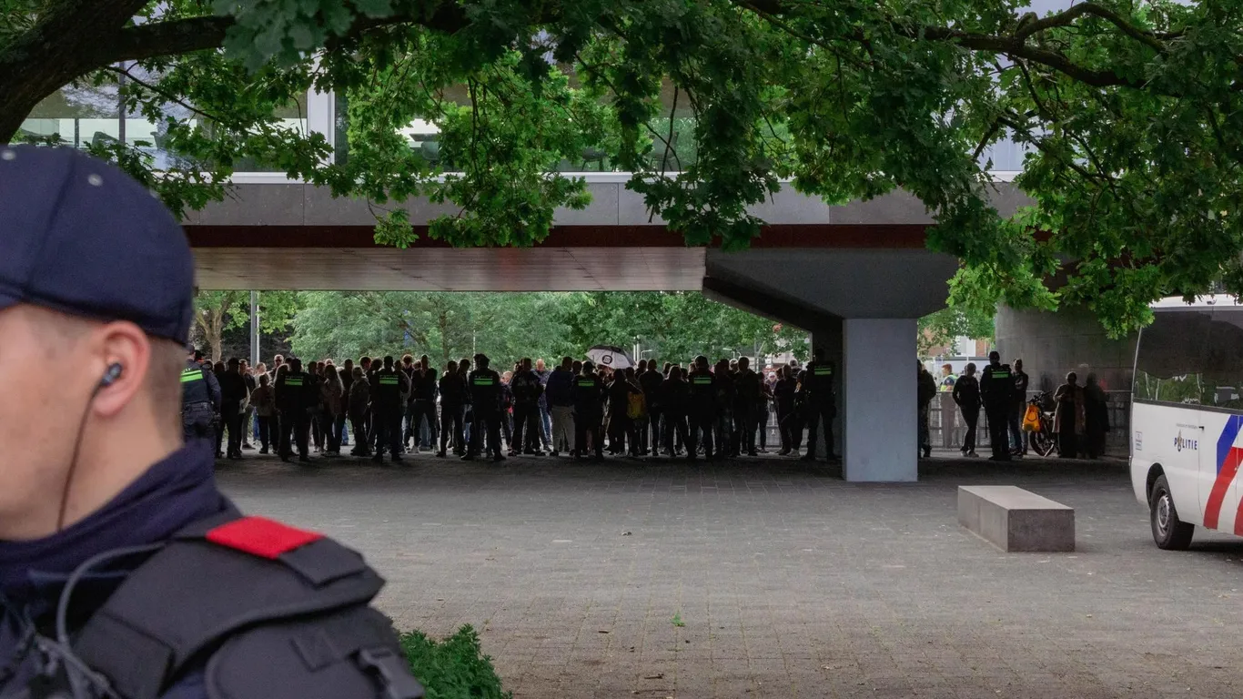 Demonstranten tegen de komst van een asielzoekerscentrum zijn in de verte zichtbaar bij het provinciehuis, achter een politielinie