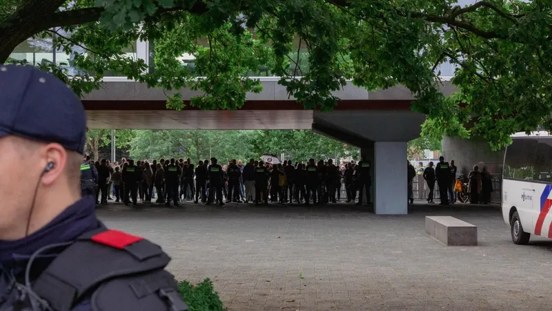 Demonstranten tegen de komst van een asielzoekerscentrum zijn in de verte zichtbaar bij het provinciehuis, achter een politielinie