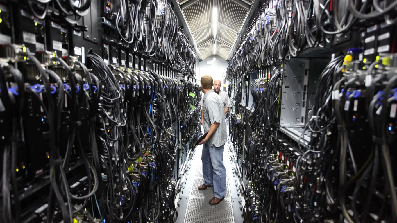 In het gangpad van een datacentrum, tussen een lange rij aan apparaten en kabels