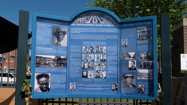 Het monument op de Haagse Markt: een bord bestaand uit drie delen met daarop foto's van en verhalen over diverse communistische verzetsstrijders, waarvan vooral Anton de Kom goed zichtbaar is.