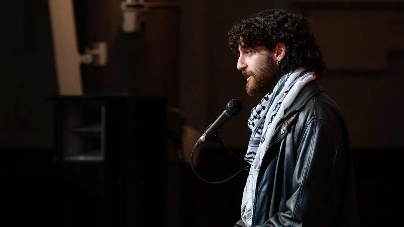 Sahand Mozdbar staat met een kufiyeh om achter de spreekstoel