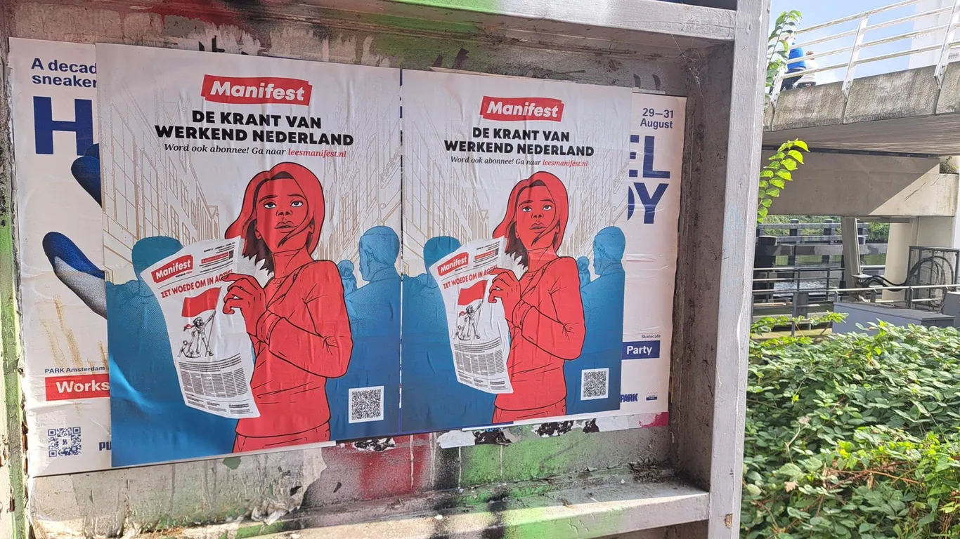 Posters hangen op een aanplakplaats. Daarop leest een strijdbare vrouw de krant Manifest, met daarboven de leus "Manifest - de krant van werkend Nederland'