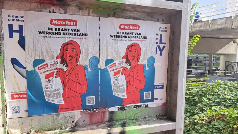 Posters hangen op een aanplakplaats. Daarop leest een strijdbare vrouw de krant Manifest, met daarboven de leus "Manifest - de krant van werkend Nederland'
