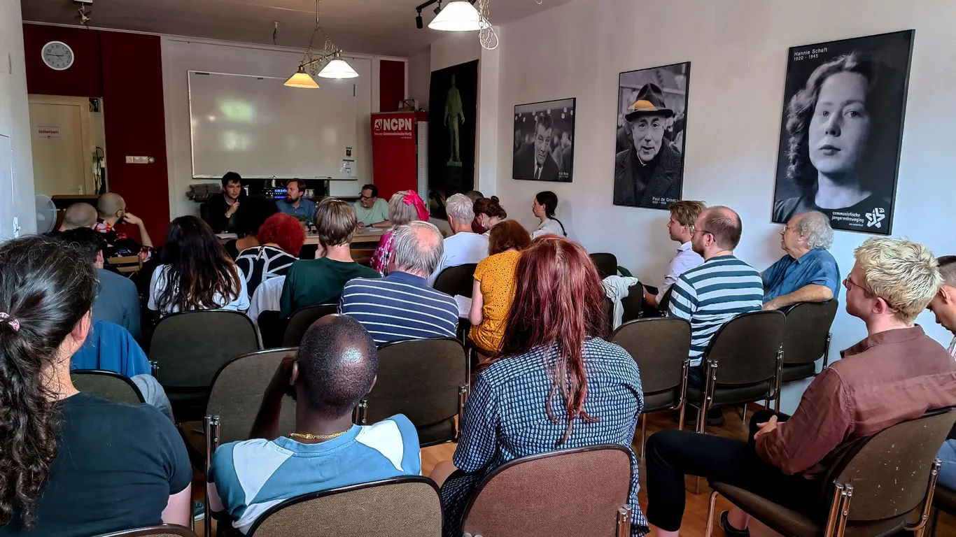 Gedelegeerden doen mee aan een gesprek op de partijconferentie van de NCPN. Op de muur hangen foto's van Hannie Schaft, Paul de Groot en Fré Meis