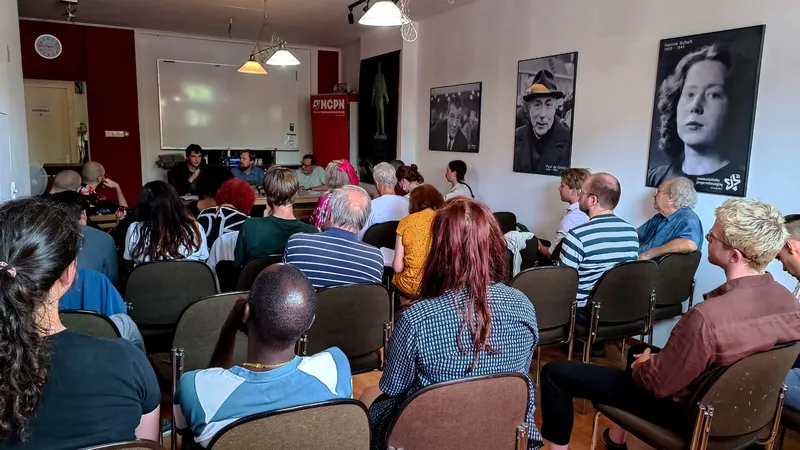Gedelegeerden doen mee aan een gesprek op de partijconferentie van de NCPN. Op de muur hangen foto's van Hannie Schaft, Paul de Groot en Fré Meis
