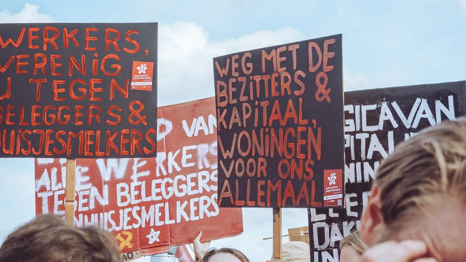 Diverse protestborden op een woondemonstratie, met voorop "Werkers, verenig u tegen beleggers & huisjesmelkers" en "Weg met de bezitters & kapitaal, woningen voor ons allemaal!"