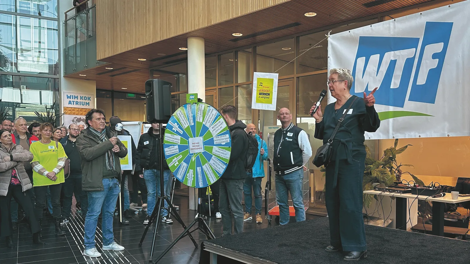 FNV-personeel staakte in februari. Een vrouw staat op het podium met achter haar het logo van de FNV, maar dan met de letters "WTF".
