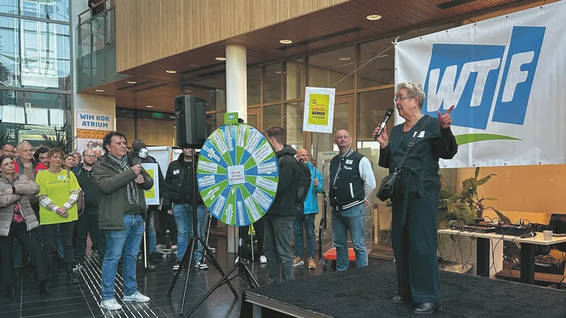 FNV-personeel staakte in februari. Een vrouw staat op het podium met achter haar het logo van de FNV, maar dan met de letters "WTF".