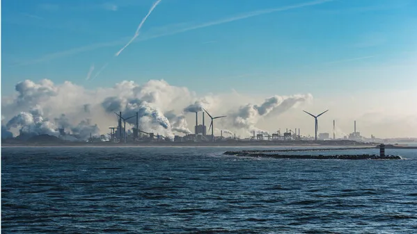 Een foto vanaf de zee, met op de achtergrond TATA Steel omgeven door stoom- en rookwolken.