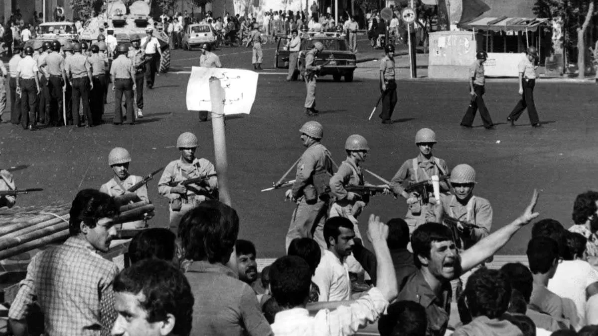 Iraanse oliewerkers tijdens een staking in 1978. Daarachter een aantal militairen die hun wapens op hen mikken.