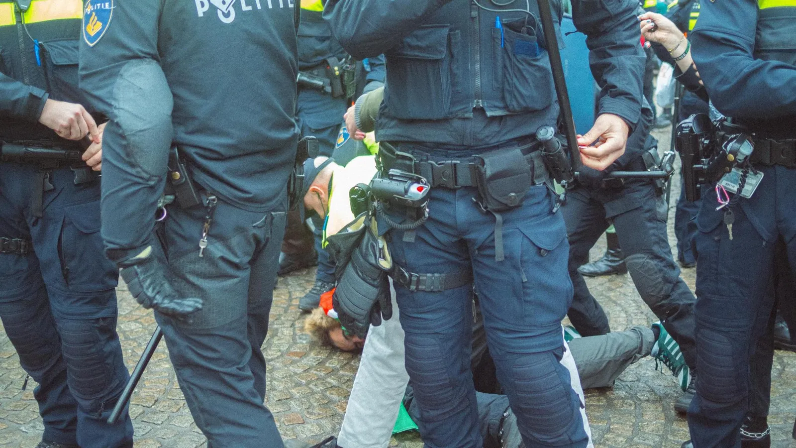 Een persoon wordt op de Dam hardhandig tegen de grond gewerkt door de politie tijdens een demonstratie na de rellen van Israëlische 'voetbalsupporters'.