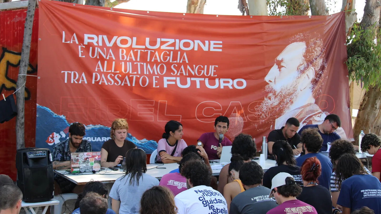 Deelnemers aan het seminar zitten voor een spandoek met een foto van Fidel Castro, die leest: "De revolutie is een strijd op leven of dood tussen het verleden en de toekomst"
